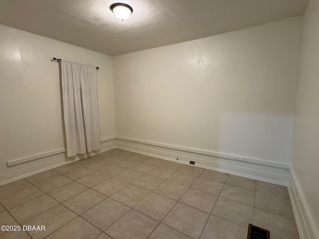 empty room featuring a textured ceiling, light tile patterned flooring, visible vents, and baseboards