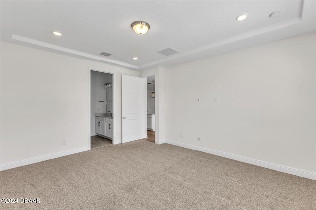 unfurnished bedroom featuring carpet floors, connected bathroom, and a tray ceiling