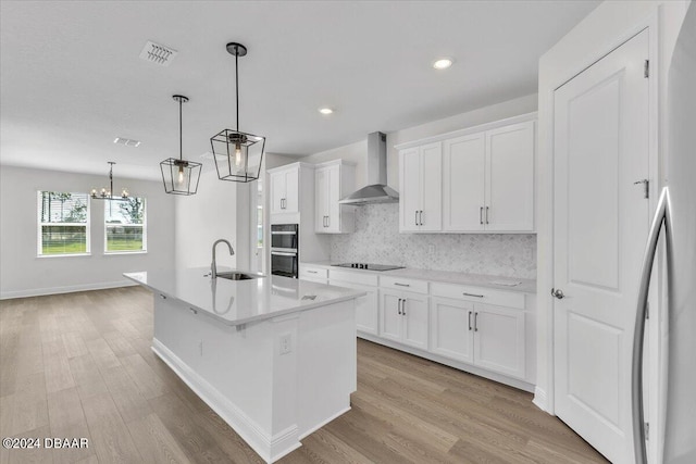 kitchen with white cabinetry, wall chimney exhaust hood, and a kitchen island with sink