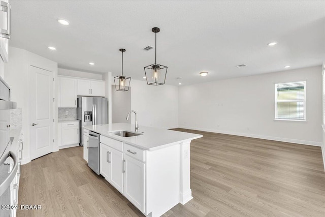 kitchen featuring sink, a center island with sink, white cabinets, light hardwood / wood-style floors, and hanging light fixtures