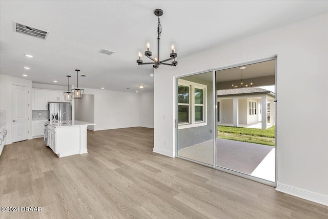 kitchen with pendant lighting, stainless steel fridge, light hardwood / wood-style floors, and a kitchen island with sink