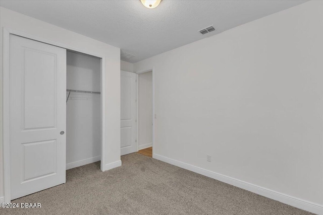 unfurnished bedroom with a textured ceiling, light carpet, and a closet