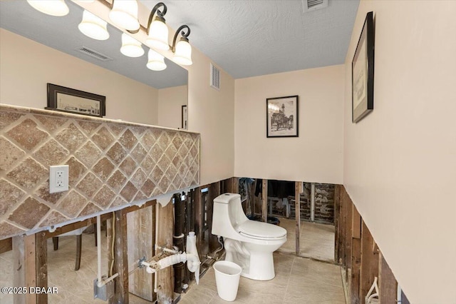 bathroom featuring tile patterned floors, toilet, a textured ceiling, and a notable chandelier