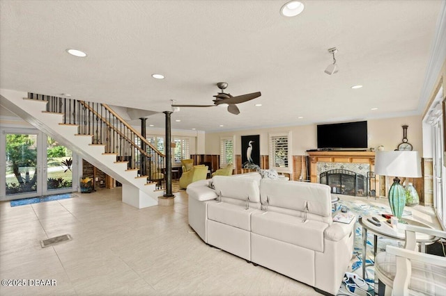 living room featuring ceiling fan, a healthy amount of sunlight, a tiled fireplace, and a textured ceiling