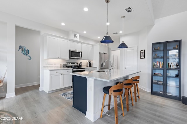 kitchen with a center island with sink, appliances with stainless steel finishes, light wood-style floors, white cabinets, and a sink