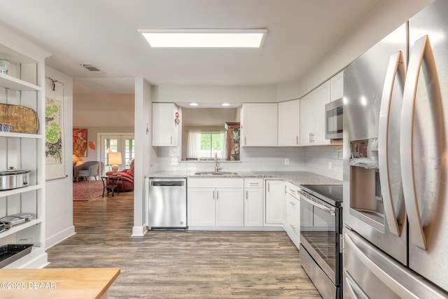 kitchen with white cabinets, appliances with stainless steel finishes, decorative backsplash, sink, and light wood-type flooring