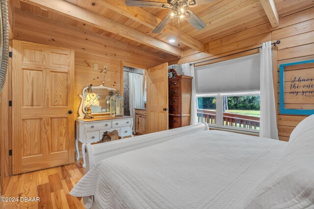 bedroom with wood walls, beamed ceiling, ceiling fan, wood ceiling, and light hardwood / wood-style flooring