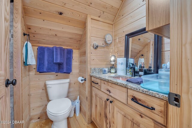 bathroom with hardwood / wood-style floors, vanity, wooden walls, toilet, and vaulted ceiling