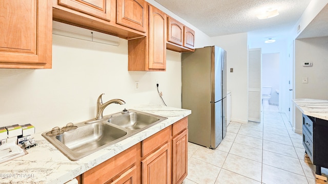 kitchen featuring light tile patterned floors, a textured ceiling, sink, and stainless steel fridge