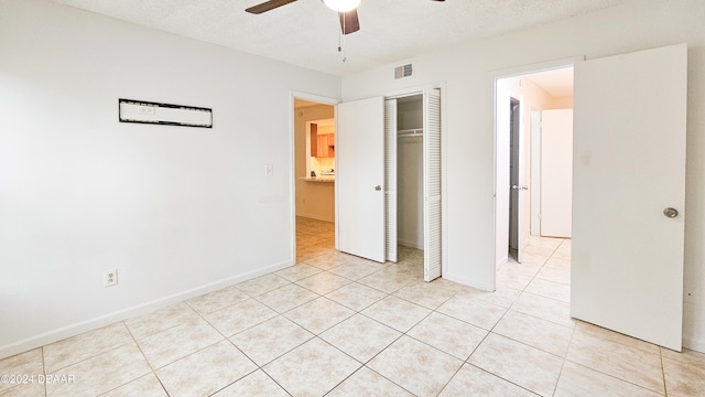 unfurnished bedroom with light tile patterned flooring, ceiling fan, a textured ceiling, and a closet