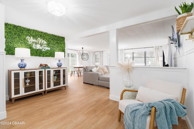 living room featuring light wood-type flooring, an inviting chandelier, and beamed ceiling