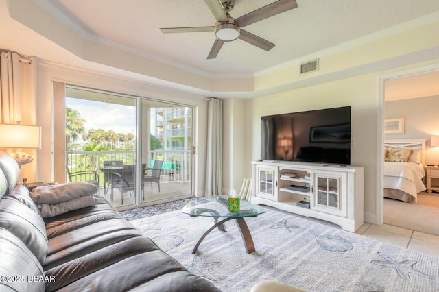 tiled living room with ornamental molding, ceiling fan, and a tray ceiling