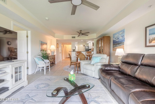 living room featuring a raised ceiling, ornamental molding, light tile patterned floors, and ceiling fan