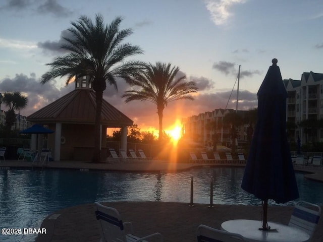 pool at dusk featuring a patio and a water view