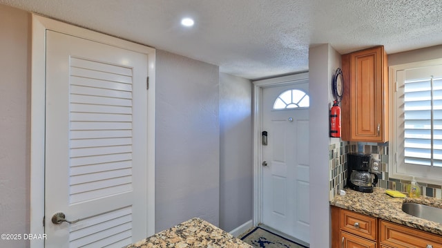 interior space with decorative backsplash, sink, light stone countertops, and a textured ceiling