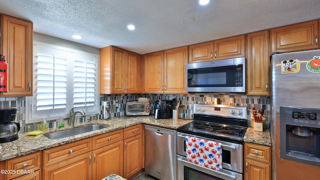 kitchen with decorative backsplash, appliances with stainless steel finishes, light stone counters, a textured ceiling, and sink