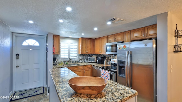 kitchen with appliances with stainless steel finishes, a textured ceiling, light stone counters, and sink