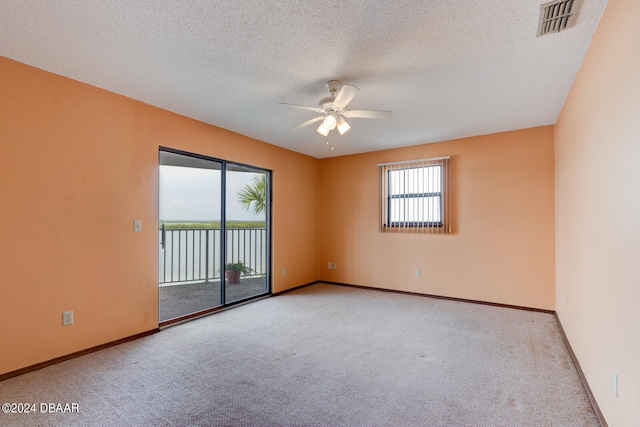 empty room featuring ceiling fan, a textured ceiling, a water view, and light colored carpet