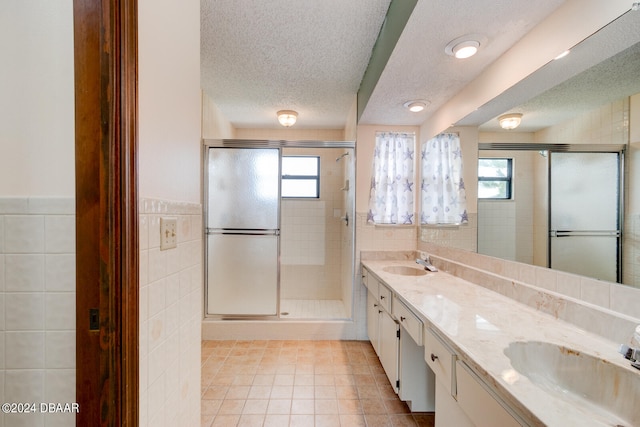 bathroom featuring tile patterned flooring, a textured ceiling, vanity, a shower with shower door, and tile walls