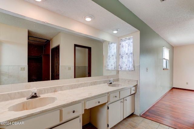 bathroom with wood-type flooring, vanity, a textured ceiling, and tile walls