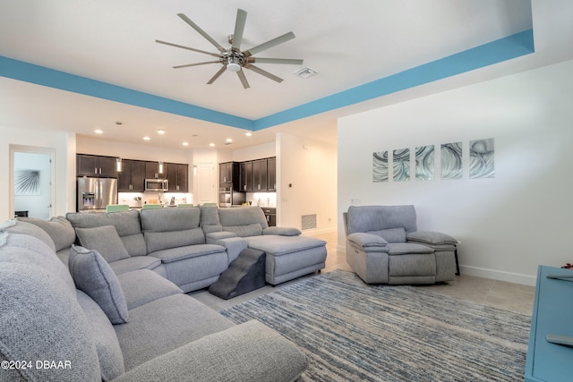 living room featuring ceiling fan, a tray ceiling, and light tile patterned floors