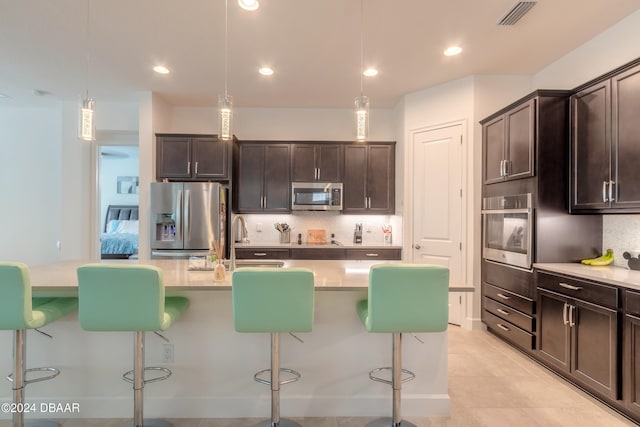 kitchen featuring dark brown cabinets, a center island with sink, decorative light fixtures, and appliances with stainless steel finishes