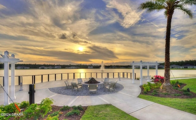 patio terrace at dusk with a yard, a pergola, a water view, and a fire pit