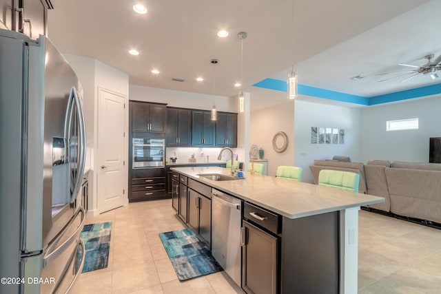 kitchen with sink, an island with sink, backsplash, appliances with stainless steel finishes, and decorative light fixtures