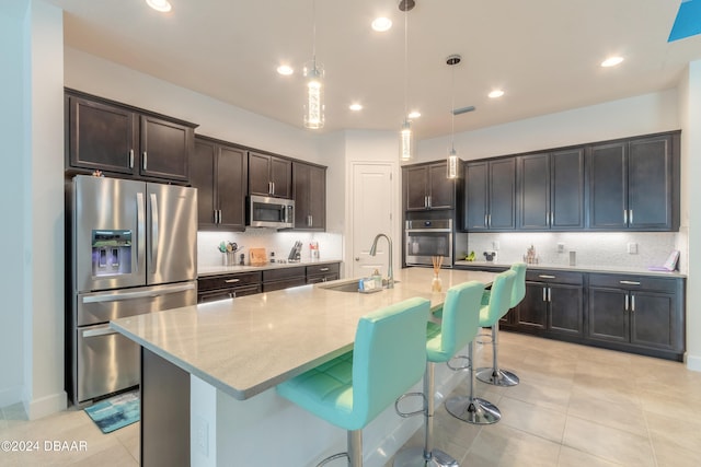 kitchen featuring sink, appliances with stainless steel finishes, a breakfast bar area, decorative light fixtures, and a kitchen island with sink