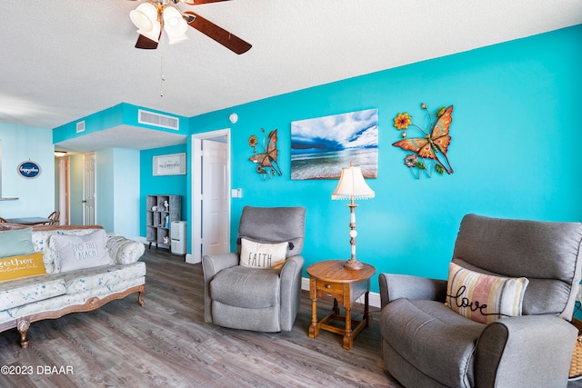 living room with a textured ceiling, wood-type flooring, and ceiling fan