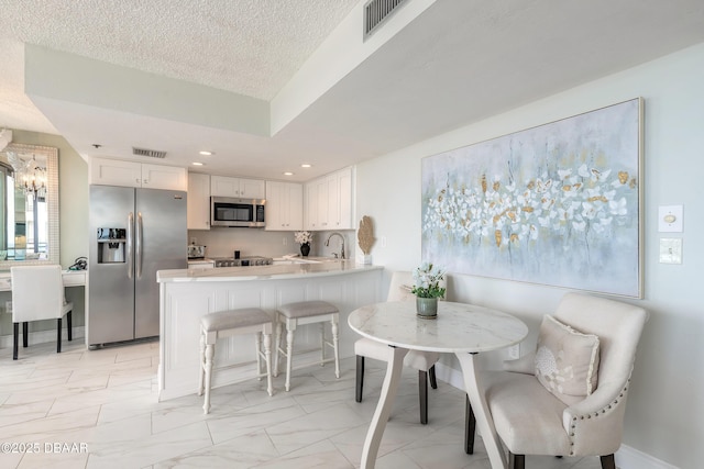 kitchen with white cabinets, appliances with stainless steel finishes, a breakfast bar, a peninsula, and light countertops