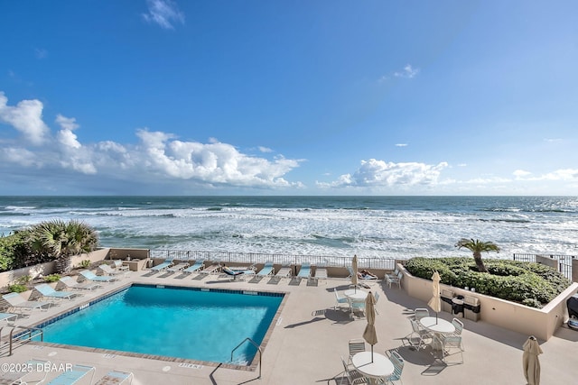 pool with a patio, a water view, and fence