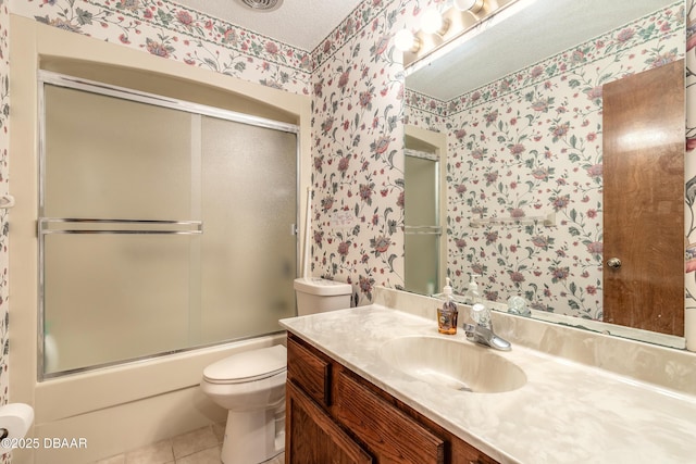 bathroom with wallpapered walls, toilet, tile patterned floors, vanity, and bath / shower combo with glass door