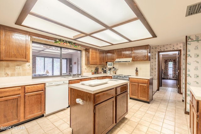 kitchen featuring white dishwasher, wallpapered walls, a sink, light countertops, and tasteful backsplash