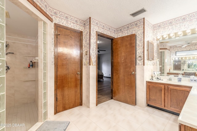 full bath featuring wallpapered walls, tiled shower, a textured ceiling, tile patterned floors, and vanity