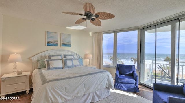 bedroom featuring a textured ceiling, floor to ceiling windows, access to exterior, a water view, and ceiling fan