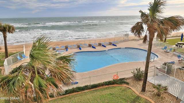 view of swimming pool featuring a patio area, a water view, and a view of the beach