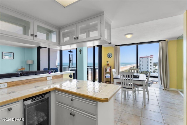 kitchen with wine cooler, light tile patterned floors, white cabinets, tile countertops, and kitchen peninsula