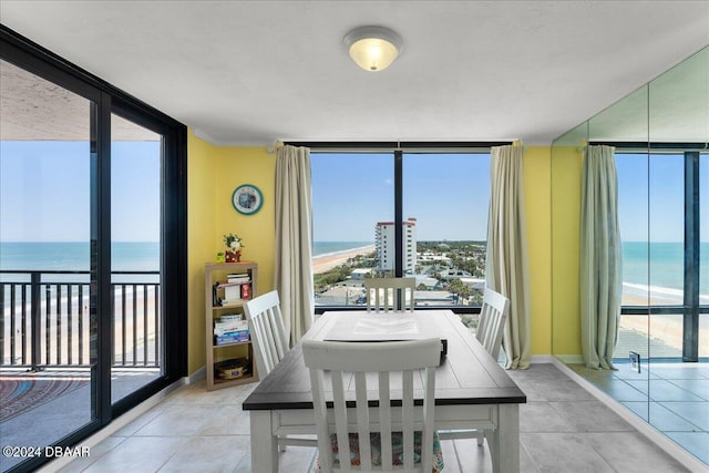 dining space featuring expansive windows, a view of the beach, light tile patterned floors, and a water view