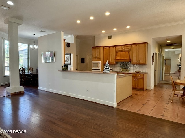 kitchen featuring white microwave, light hardwood / wood-style flooring, decorative backsplash, custom range hood, and decorative columns