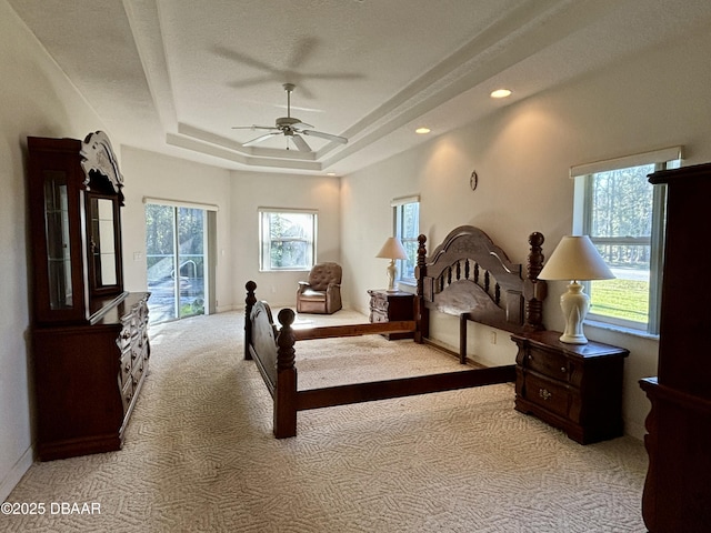 carpeted bedroom featuring a tray ceiling, access to exterior, and ceiling fan