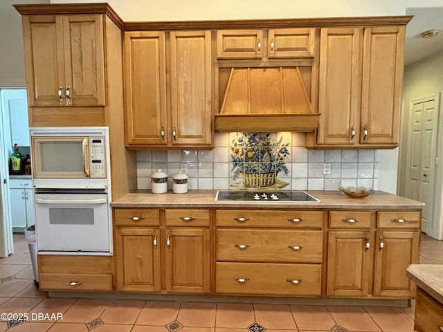 kitchen featuring custom range hood, white appliances, light tile patterned floors, and backsplash