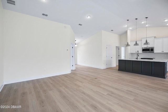 kitchen featuring light wood-type flooring, hanging light fixtures, an island with sink, and white cabinets