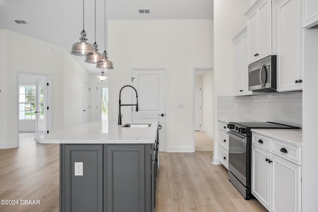 kitchen featuring stainless steel appliances, light hardwood / wood-style floors, white cabinetry, an island with sink, and pendant lighting