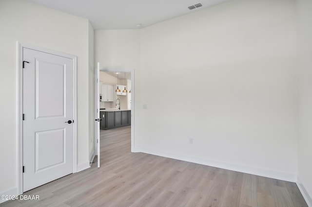 spare room with light hardwood / wood-style floors, sink, and a notable chandelier