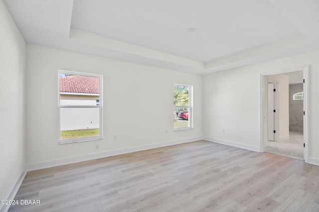 unfurnished room with light wood-type flooring and a tray ceiling