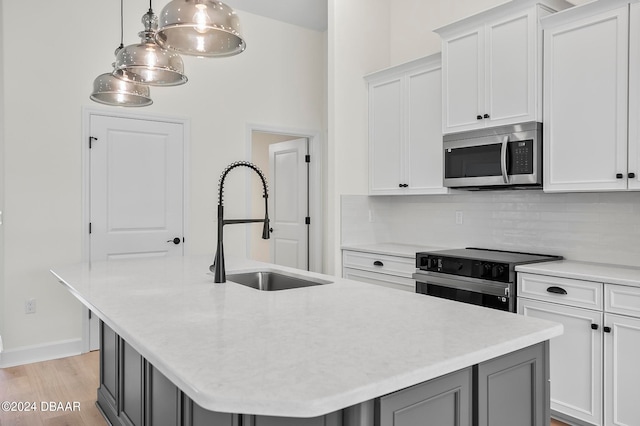 kitchen featuring stainless steel appliances, a center island with sink, decorative light fixtures, and white cabinets