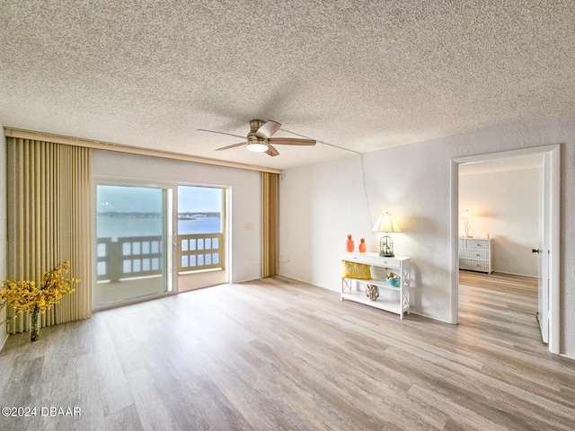 empty room featuring a textured ceiling, light hardwood / wood-style floors, ceiling fan, and a water view