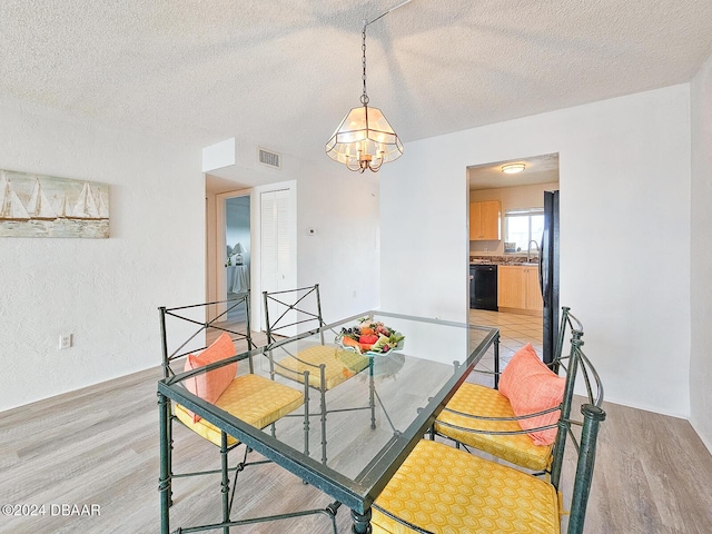 dining room featuring a textured ceiling, light hardwood / wood-style floors, an inviting chandelier, and sink