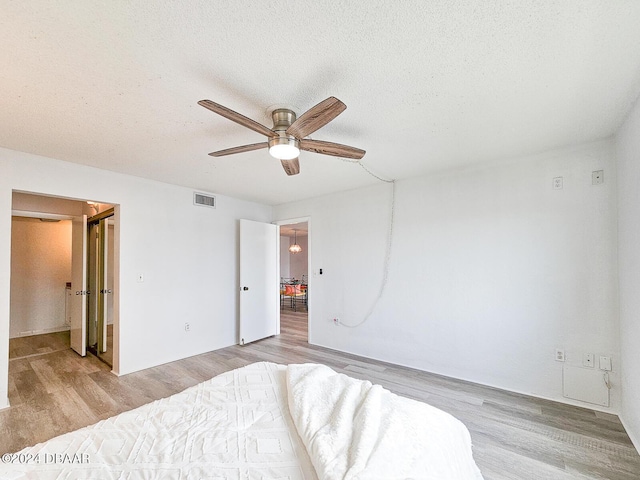 bedroom with ceiling fan, light hardwood / wood-style floors, a textured ceiling, and ensuite bath